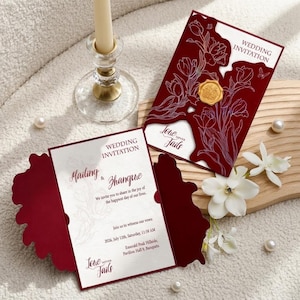 Peut inclure: Invitation de mariage bordeaux avec un motif floral et un sceau de cire doré. L'invitation présente le texte "Wedding Invitation", "Mailing & Zhangue" et "Love Never Fails". Comprend des fleurs blanches et des perles.
