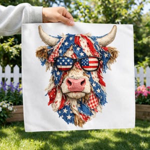 Op de afbeelding: Een witte vierkante handdoek met een Highland-koeienontwerp met patriottische rode, witte en blauwe accenten. De koe draagt een zonnebril met het Amerikaanse vlagontwerp. De vacht van de koe is versierd met sterren en strepen.