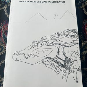 以下が含まれることがあります： ROLF BORZIK und DAS TANZTHEATERというタイトルの白いブックカバー。手前には黒いインクの線画で描かれたワニの頭があり、上半分には2つの単純な三角形のピラミッドの形と小さなヤシの木が背景に描かれています。
