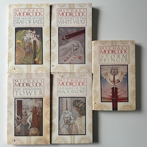 May include: A selection of Michael Moorcock's Elric Saga books. The covers display fantasy illustrations, with titles such as "The Weird of the White Wolf" and "The Vanishing Tower." The books are arranged on a neutral background.