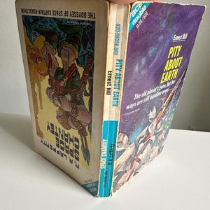 Może przedstawiać: Trzy książki w miękkiej oprawie science fiction w stylu vintage są trzymane pod kątem. Okładki zawierają kolorowe ilustracje i tytuły takie jak "Space Chantey" i "Pity About Earth". Książki są w dobrym stanie, z widocznymi śladami zużycia na krawędziach.