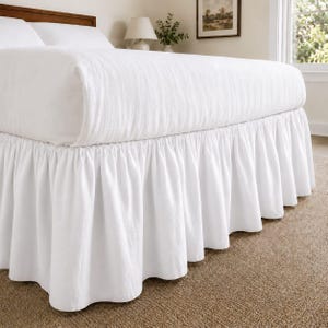 May include: A white bed valance featuring a gathered, ruffled design that extends from the base of the mattress to the floor. The fabric is solid white with a soft texture, creating a layered appearance around the lower perimeter of the bed frame.