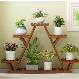 May include: A wooden plant stand with multiple shelves in a triangular design. The stand is filled with various potted plants, including succulents, flowering plants, and leafy greens. The pots are white and the wood is a warm brown color.