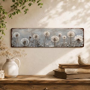 May include: A rectangular metal wall sign featuring a horizontal panoramic print of white dandelion seed heads against a weathered, mottled gray background. The sign has rounded corners with small holes for mounting and a distressed, rusted edge.