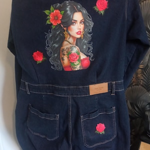 Peut inclure: Combinaison en jean bleu foncé avec une illustration colorée d'une femme avec des fleurs dans les cheveux et un tatouage de rose. Broderie de roses rouges sur les poches arrière et le dos de la combinaison.