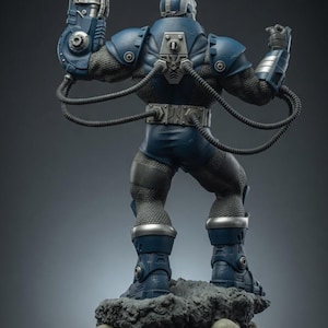 May include: A detailed statue of a blue and silver armored figure, standing on a rocky base with skulls. The figure has a mechanical arm and various tubes connected to its body. The statue is a collectible item.