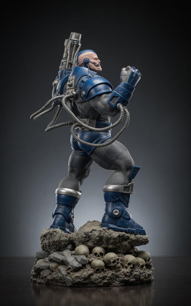 May include: A detailed statue of a muscular, blue-armored figure with a bald head and a grimacing expression. The figure stands on a rocky base with skulls, and has a large weapon on its back. The statue is a collectible item.