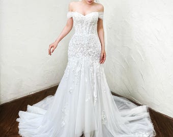 Vestido de novia romántico estilo sirena con hombros descubiertos, encaje floral en 3D y cola de tul.