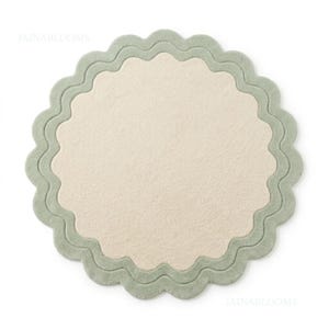 May include: A circular rug featuring a solid cream-colored center and a wide, scalloped sage green border. The textile surface has a soft, uniform texture throughout. The text JAINABLOOMS is visible in the upper left and lower right corners.