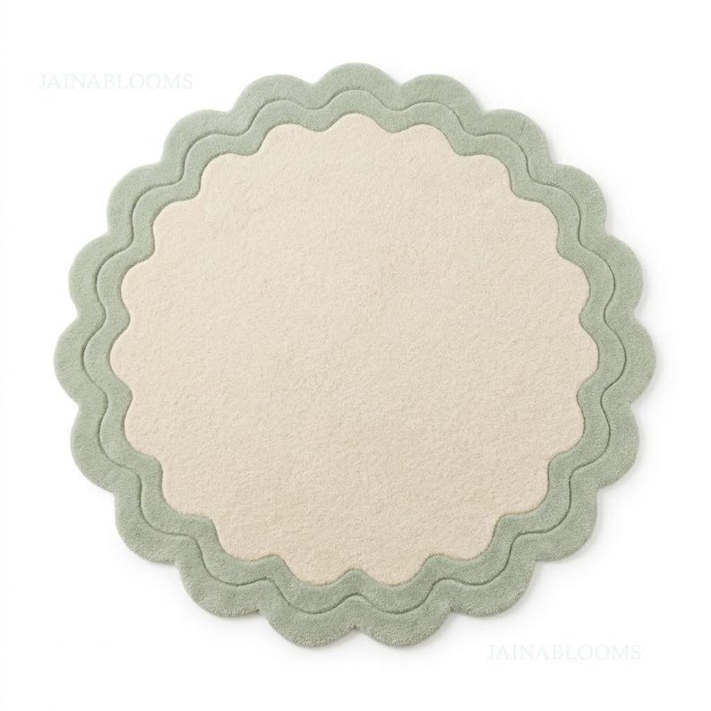 May include: A circular rug featuring a solid cream-colored center and a wide, scalloped sage green border. The textile surface has a soft, uniform texture throughout. The text JAINABLOOMS is visible in the upper left and lower right corners.