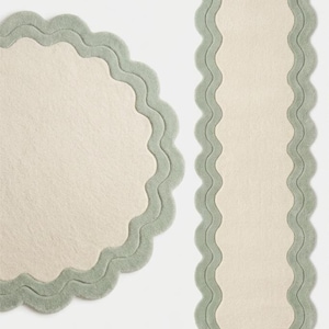 May include: A circular rug and a rectangular runner rug, both featuring a cream-colored center and a wide, sage green scalloped border. The edges of both rugs have a wavy, undulating design that frames the central cream-colored surface area.