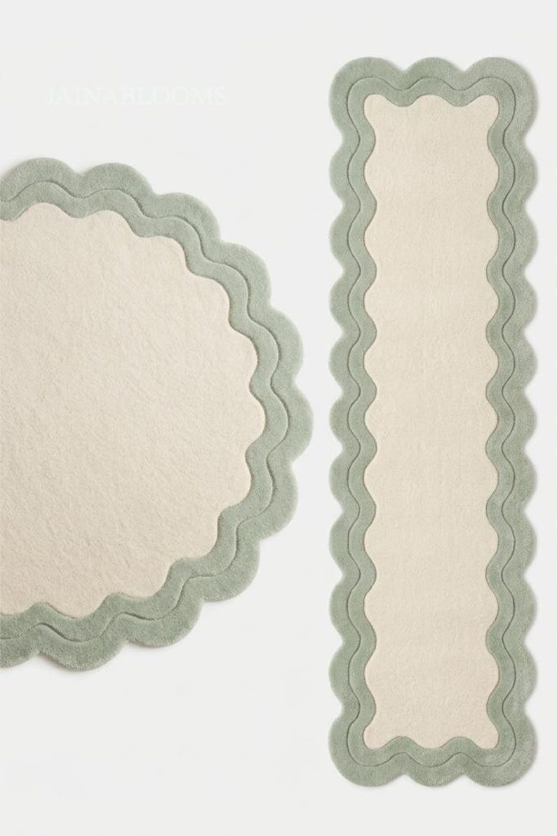 May include: A circular rug and a rectangular runner rug, both featuring a cream-colored center and a wide, sage green scalloped border. The edges of both rugs have a wavy, undulating design that frames the central cream-colored surface area.