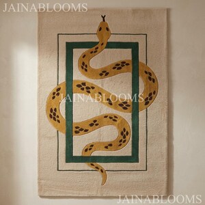 May include: A rectangular beige rug featuring a central dark green rectangular border. A yellow snake with dark brown diamond-shaped markings is depicted winding through the green frame. The text JAINABLOOMS is visible at the top and bottom.