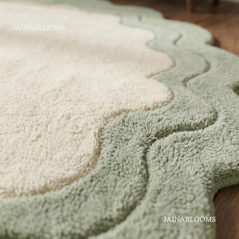 May include: A plush area rug featuring a cream-colored center and a wide, sage green scalloped border. The rug has a thick, tufted texture throughout. The text JAINABLOOMS is visible in the upper left and lower right corners of the image.