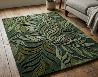 Puede incluir: Una alfombra rectangular con un fondo verde bosque profundo y un patrón texturizado en relieve de grandes hojas botánicas en tonos más claros de verde oliva y salvia, con el texto JAINABLOOMS visible sobre la alfombra.