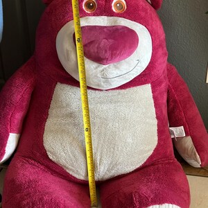 May include: A large, plush, pink teddy bear with a white belly and a heart-shaped nose. The bear is approximately 30 inches tall. It has a grumpy expression and is a character from a popular animated film.