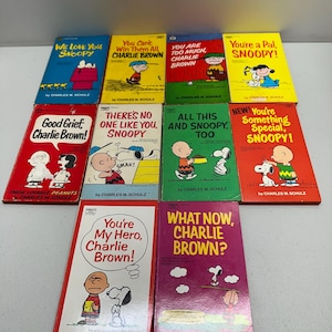 May include: A collection of vintage Peanuts comic books featuring Charlie Brown and Snoopy. The books have colorful covers with titles like "Good Grief, Charlie Brown!" and "You're a Pal, Snoopy!" by Charles M. Schulz.