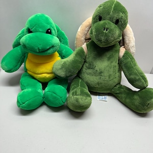 May include: Two plush turtle toys. One is bright green with a yellow belly. The other is a darker green with a tan shell. Both have soft, stuffed bodies and friendly expressions. These toys are suitable for children.