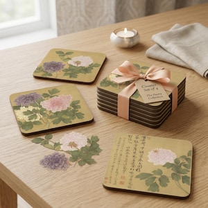 Puede incluir: Un juego de cuatro posavasos cuadrados con ilustraciones de peonías en rosa, morado y blanco sobre fondo dorado. Un posavasos muestra caligrafía china negra. El conjunto está atado con una cinta rosa claro y una etiqueta que dice Coaster Set of 4 The Peony Collection.