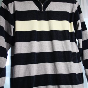 May include: A striped long-sleeve shirt with a black and gray color scheme. The shirt has a light yellow stripe across the chest and a mock neck collar.