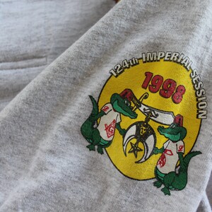 May include: A gray t-shirt with a yellow circle graphic featuring two green alligators holding a Masonic symbol. The circle also includes the text "124th IMPERIAL SESSION 1998".