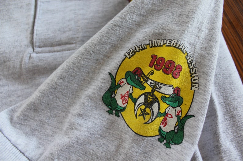 May include: A gray t-shirt with a yellow circle graphic featuring two green alligators holding a Masonic symbol. The circle also includes the text "124th IMPERIAL SESSION 1998".