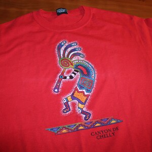 May include: Red t-shirt with a colorful graphic of a Native American flute player and the text "Canyon de Chelly".