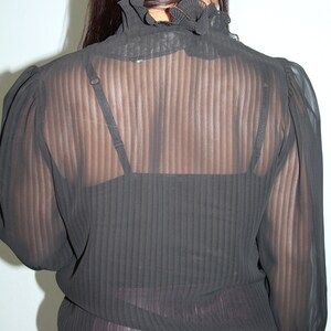 May include: Black sheer blouse with a ruffled collar and long sleeves. The blouse is made of a lightweight fabric and has a striped pattern.