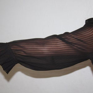 May include: A black sheer blouse with long sleeves and a ruffled cuff. The blouse has a striped pattern.