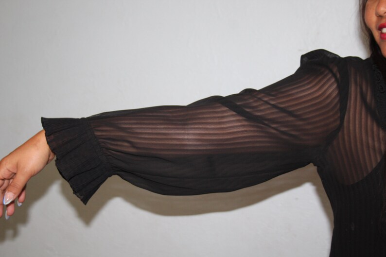 May include: A black sheer blouse with long sleeves and a ruffled cuff. The blouse has a striped pattern.