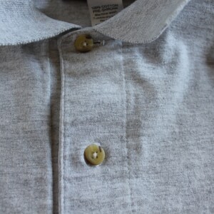 May include: A gray polo shirt with a button-up closure and a small Mickey Mouse design on the right side. The shirt is made of 100% cotton.