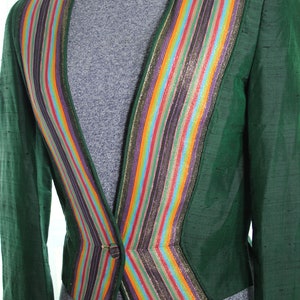 Op de afbeelding: Een groene blazer met een kleurrijke gestreepte bies. De bies is gemaakt van meerdere kleuren, waaronder goud, paars, oranje en blauw. De blazer heeft een enkele knoopsluiting.