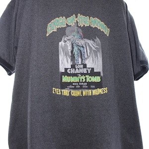 May include: A dark gray t-shirt with a vintage movie poster design featuring Lon Chaney in "The Mummy's Tomb". The poster has a green and yellow color scheme and the text "Curse of the Mummy" and "Eyes that crawl with madness".