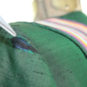 Op de afbeelding: Een close-up van een groene stof met een kleine scheur. De stof heeft een regenboogstreep langs de rand.