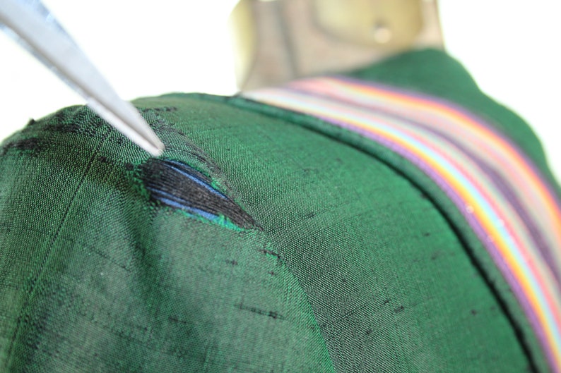 Op de afbeelding: Een close-up van een groene stof met een kleine scheur. De stof heeft een regenboogstreep langs de rand.