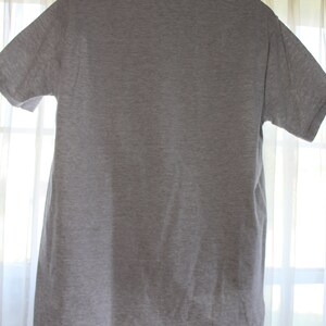 May include: A plain gray t-shirt with a collared neckline. The shirt is hanging on a hanger.