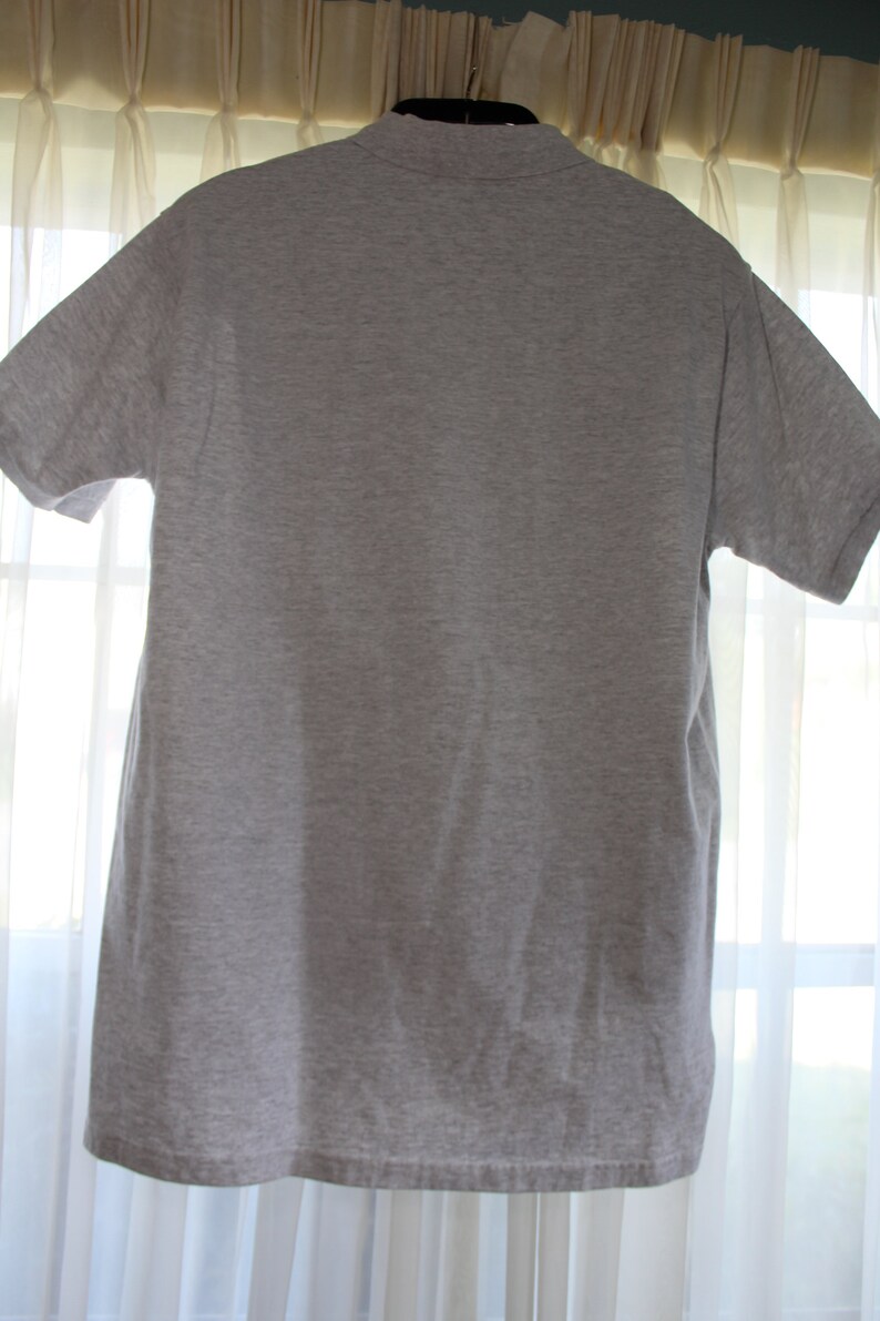 May include: A plain gray t-shirt with a collared neckline. The shirt is hanging on a hanger.