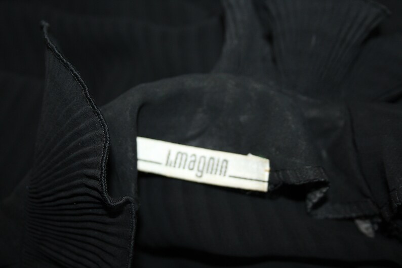 May include: Black pleated fabric with a white label that reads "L.Magnin".
