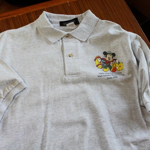 May include: Gray polo shirt with a Mickey Mouse graphic and the text "125th Anniversary Celebration Walt Disney World Resort June 1998".