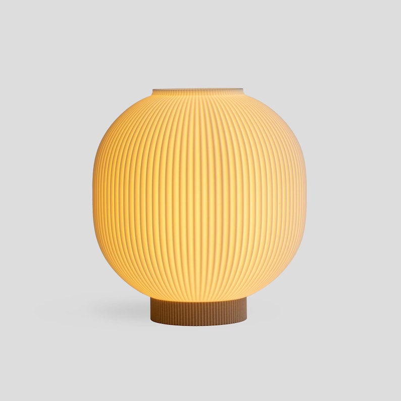 May include: A modern, spherical table lamp with a ribbed, off-white shade. The lamp sits on a brown, cylindrical base. The shade emits a warm, inviting glow, perfect for ambient lighting in a living room or bedroom.
