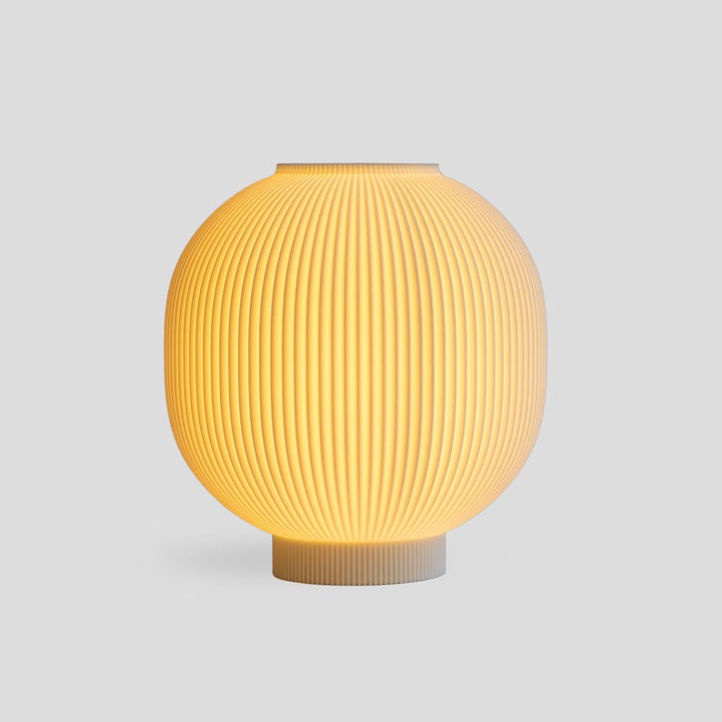 May include: A modern, spherical table lamp with a ribbed, off-white shade. The lamp has a warm, yellow glow emanating from within. The base is a matching off-white color and has a cylindrical shape. The lamp is a stylish home decor item.