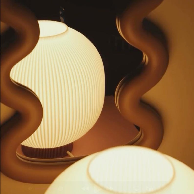 May include: A pair of modern pendant lights with a warm glow. The lampshades are white and ribbed, with a rounded shape. The fixtures are supported by curved, brown metal structures, creating a unique design. The background is a soft, neutral color.