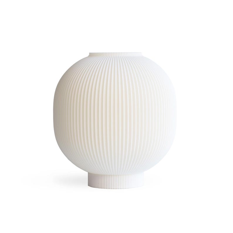 May include: A white, ribbed ceramic vase with a rounded body and a cylindrical base. The vase has a narrow opening at the top and a series of vertical ridges that run from top to bottom. The design is minimalist and modern.