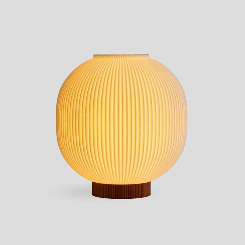 May include: A spherical table lamp with a ribbed, off-white shade. The lamp sits on a dark brown, cylindrical base. The lamp emits a warm, inviting glow, suggesting it is turned on. The design is modern and minimalist.