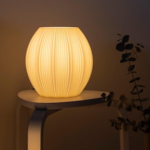 May include: A spherical table lamp with a ribbed, off-white surface that emits a warm, soft glow. The lamp features a rounded, bulbous shape with vertical ridges running from the top opening to the base, creating a textured, light-diffusing effect.
