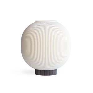 May include: A white, ribbed, spherical vase with a dark gray base. The vase has a rounded shape with vertical ridges, and the base is a solid, cylindrical form. The design is minimalist and modern, suitable for home decor.