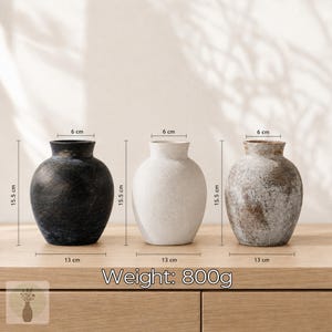 May include: Three vases with a textured finish, each measuring 15.5 cm in height, 13 cm in width, and 6 cm at the opening. The set includes one black, one white, and one distressed brown and white vase. Each vase has a weight of 800 grams.