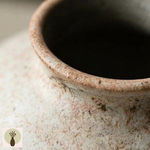 Puede incluir: Primer plano de un jarr&oacute;n de cer&aacute;mica texturizado de color blanquecino con interior oscuro. El borde es marr&oacute;n contrastante con una apariencia moteada. El jarr&oacute;n tiene una est&eacute;tica r&uacute;stica y hecha a mano.
