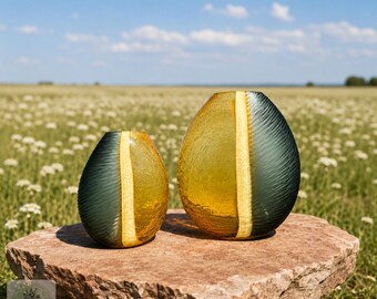 May include: Two egg-shaped glass vases with a textured, dark gray finish on the sides and a smooth, vertical amber-colored stripe down the center. The vases are rounded and feature a crackled glass appearance, displayed as a pair of different sizes.