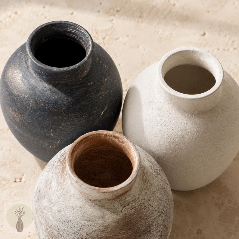 May include: Three round vases with narrow necks and wide bodies. One vase is matte black with visible brushstrokes, one is off-white with a textured finish, and one is a weathered brown with a distressed, light-colored wash over the surface.